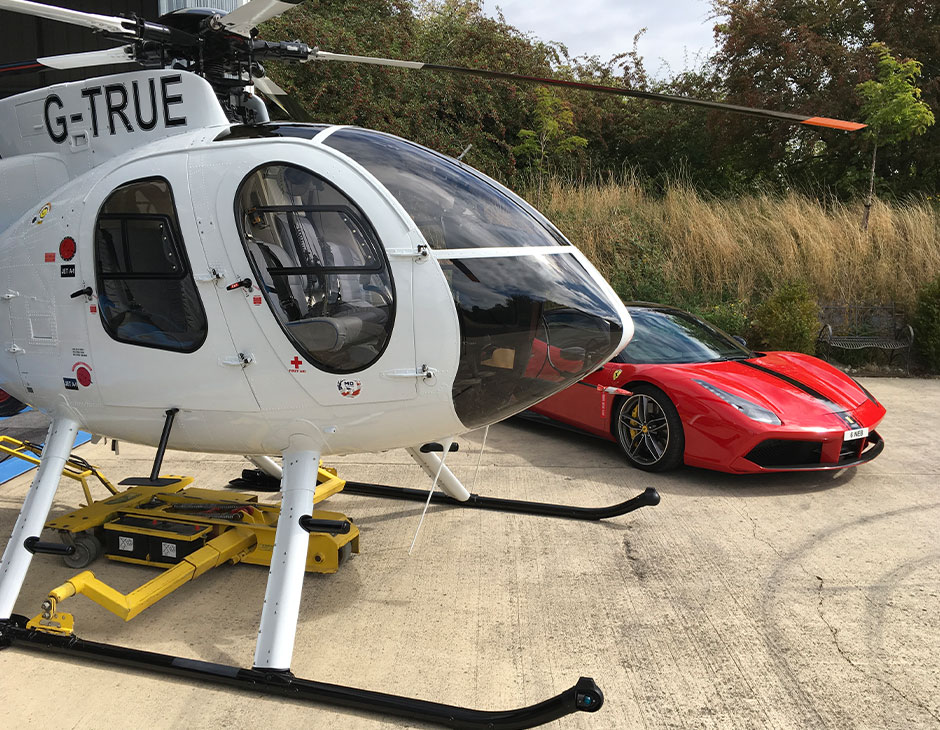 A sleek red sports car and a white helicopter with the registration 