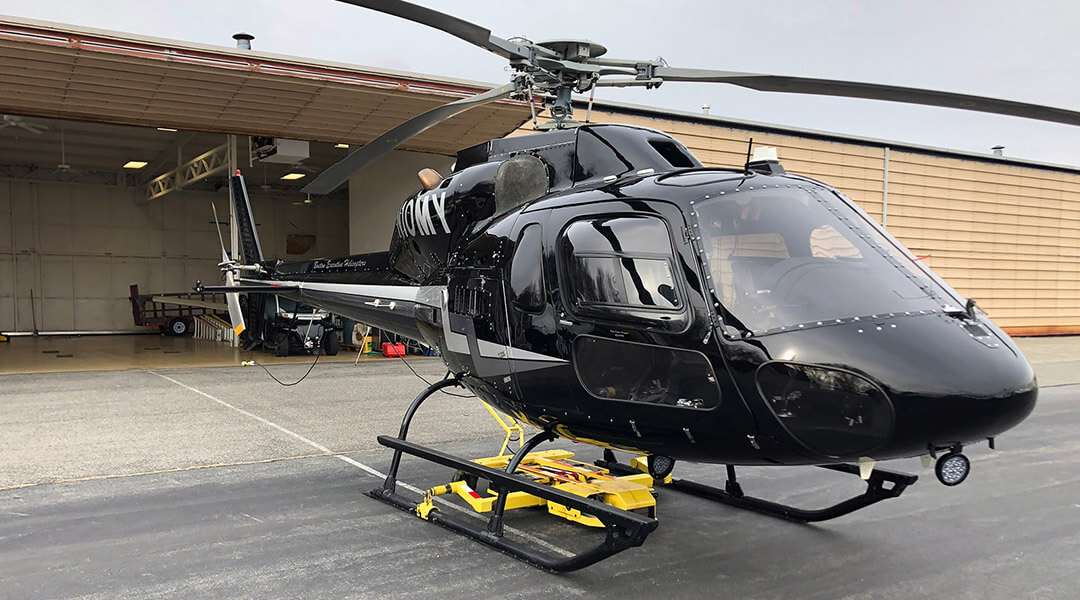 Black helicopter parked outside a hangar on an airstrip. The helicopter has